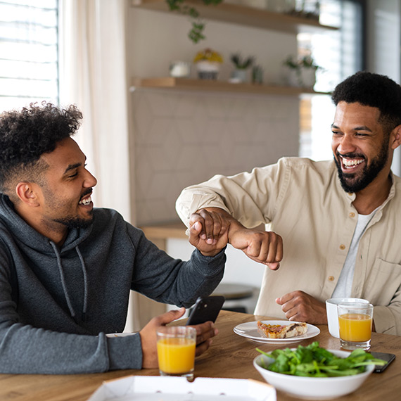 Ernährung: Zwei Männer sitzen fröhlich am Tisch und essen zusammen