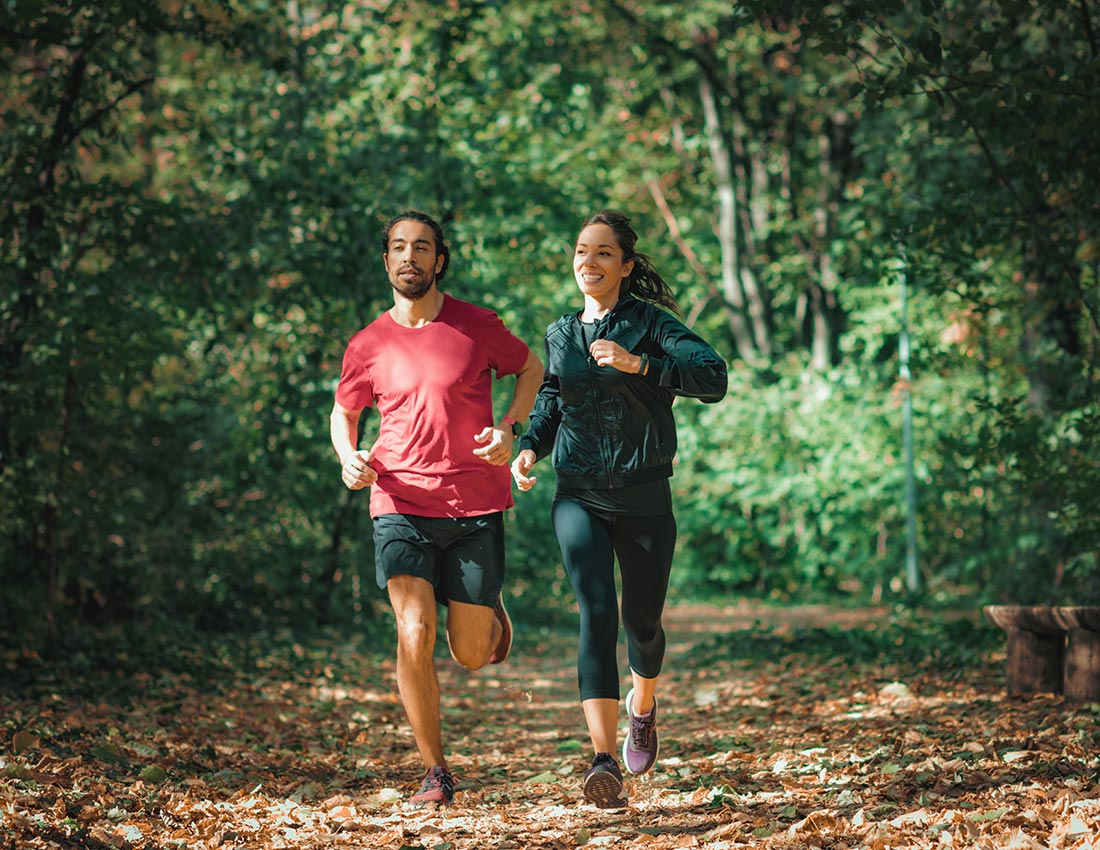 Körperliche Energie: Ein Paar joggt lachend durch den Wald