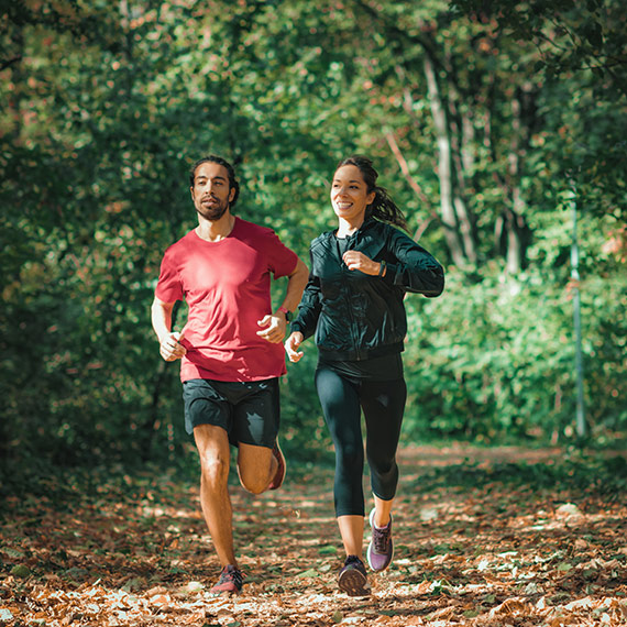 Bewegung: Ein Paar joggt lachend durch den Wald
